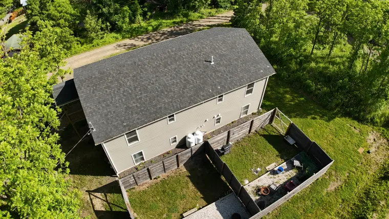 Drone view of the exterior elevation and wooded parcel edge