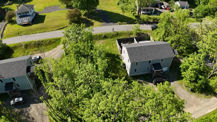 Drone image showing building exterior, yard, and wooded context